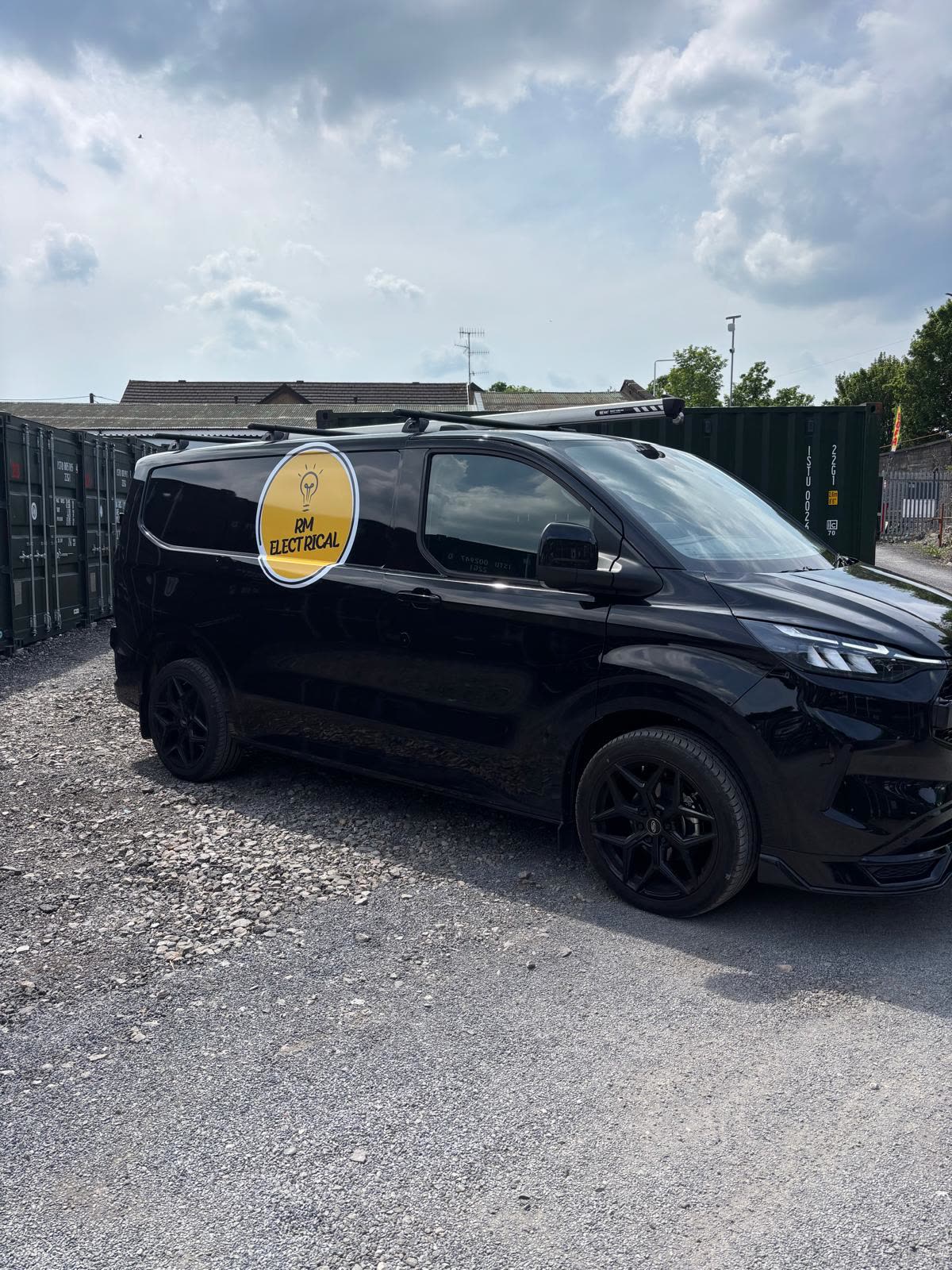 The RM Electrical van parked up on a job, black with the yellow RM roundel